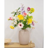 Een Kunstanemoon Real Touch paars 52cm staat op een lichte houten tafel en toont zijn realistische paarse bloemen in een beige vaas tegen een effen witte muur.