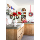 Een lichte keuken met houten kastjes, open witte planken met borden en potten, een feestelijke krans aan de muur en een Kunstbloem Amaryllis Real Touch rood 36 cm op het betonnen aanrecht.