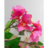 Close-up van de Kunstbloem Bougainvillea 90 cm paars: levendige paarse kunst bougainvillea bloemen met groene bladeren op een tak, tegen een zachte, lichte achtergrond.
