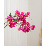 De Kunstbloem Bougainvillea 90 cm paars, met levendige paarse bloemen en groene bladeren, wordt getoond tegen een lichte neutrale achtergrond naast een houten ladder aan de rechterkant.