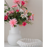 Een Kunstbloem Dahlia 68 cm roze in een witte vaas staat naast een schaal van wit keramiek met ruches op een wit oppervlak, tegen een effen lichte achtergrond.