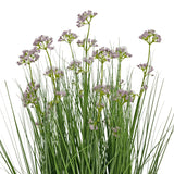 De Kunstgras Prei Bloem Ui Graspot 60cm heeft hoge, dunne groene bladeren en trossen kleine, delicate lichtpaarse bloemen op lange stelen. Het arrangement is brandvertragend en afgebeeld tegen een witte achtergrond.