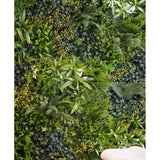Een weelderige, gestructureerde achtergrond wordt gecreëerd door de Kunsthaag Freshness 100x100 cm UV verticale tuinmuur, dichtbegroeid met groen gebladerte. Rechtsonder zijn twee gevouwen beige handdoeken zichtbaar.