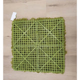 De Kunsthaag Nordic Mos 50x50 cm UV is een groene kunstgrasmat met een zichtbare kunststof rasterrug, ideaal voor luxe interieurs of het creëren van een groene muur. Hij rust op een lichte houten vloer met een klein wit label in een hoek.