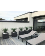 Modern terras met twee grijze loungestoelen en vijf Kunstplant Agava Pandora 85 cm UV in bijpassende vierkante plantenbakken, gerangschikt bij een wit houten hek voor een strakke, minimalistische look.