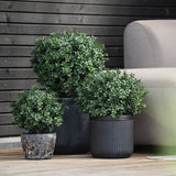 Drie Kunst Buxus op stam UV 40 cm ronde, weelderig groene potplanten staan op een houten vlonder naast een lichtgrijze buitenbank, met een donkere houten muur op de achtergrond.