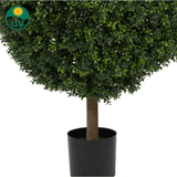 Een close-up van de Kunstplant Buxus op stam Romeinse stijl UV 95cm toont dichte groene bladeren en een bruine stam in een zwarte cilindrische pot. Een UV-beschermd symbool met een zon en "UV" tekst verschijnt in de linkerbovenhoek.