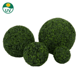 De Kunstplant Buxus Romeinse stijl UV D55cm heeft vier kunsttuibollen van verschillende grootte met dicht groen gebladerte. Een UV-label met een zonne-icoon linksboven geeft de UV-bestendigheid aan. De achtergrond is effen wit.