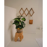 Een minimalistische kamerhoek wordt een groene oase met de Kunstplant Syngonium UV 58 cm op een krukje van natuurlijk hout, naast een bruine leren tas op een geometrisch wandrek en een witte kan, allemaal tegen gebroken witte muren en vloer.