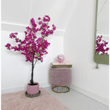 Een moderne, minimale kamerhoek met een Kunstplant Bougainvillea 125 cm Paars in een pot, een rond roze voetenbankje met gouden pootjes, gestapelde boeken, een roze kristallen bol, een wandspiegel en een zachtroze vloerkleed op een lichte vloer.