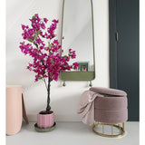 Een modern interieur met de Kunstplant Bougainvillea 125 cm Paars in een decoratieve pot, een hoge spiegel met groene lijst, een roze voetenbank met gouden voet en roze deken, en een donkere deur tegen een kraakheldere witte muur.