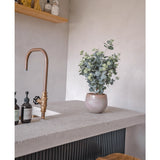 Een modern aanrecht met een bronzen kraan, zeepflessen, een houten kruk en de Kunstplant Eucalyptus 76 cm. Op de achtergrond zijn houten planken met potten en flessen gemonteerd op een lichtgrijze muur.