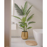 De Kunstplant Phoenix 180 cm in een gouden pot staat bij een wit bad en wastafel in een moderne minimalistische badkamer met witte muren en vloer. Vlakbij ligt een ronde geweven mat op de vloer.