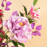 Een close-up van het Zijden kunstbloemen boeket Rosy Saga Mist, met een grote lichtpaarse pioenroos, roze lelie en paarse bladeren tegen een zachtbeige achtergrond.