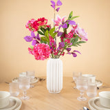 Een witte vaas van keramiek met het Zijden kunstbloemen boeket Rosy Saga Mist fleurt een houten eettafel op voor vier personen met witte borden, kommen, kopjes en glazen, tegen een effen beige muur.