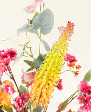 Een close-up van het levendige Zijden kunstbloemen boeket Wild Peach, met gele en oranje aarvormige bloemen met roze bloesems en groene bladeren, tegen een lichte achtergrond.