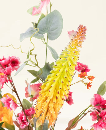 Een close-up van het levendige Zijden kunstbloemen boeket Wild Peach, met gele en oranje aarvormige bloemen met roze bloesems en groene bladeren, tegen een lichte achtergrond.