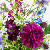 Het Zijden kunstbloemen boeket Purple Rain heeft een grote magenta dahlia, witte en paarse bloemen, blauwe bloesems en groene bladeren, die het Nederlands vakmanschap benadrukken tegen een witte achtergrond.