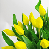 Het Zijden kunstboeket Tulpen in vaas Geel toont levendige gele tulpen met groene bladeren, prachtig gerangschikt en uitgestald tegen een effen witte achtergrond.