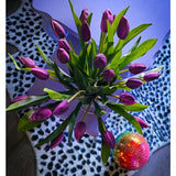 Het Zijden kunstboeket Tulpen in vaas Paars rust op een lavendelkleurige tafel naast een levendige discobal op een zwart-wit vloerkleed met luipaardprint.
