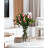 Het Zijden kunstboeket Tulpen in vaas Roze staat op een ronde witte houten tafel in een lichte, moderne woonkamer met neutrale tinten en een eigentijdse inrichting.