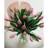 Het Zijden kunstboeket Tulpen in vaas Roze toont roze kunsttulpen met groene bladeren, gerangschikt in een glazen vaas, tentoongesteld op een wit vlak met een zacht vervaagde lichte achtergrond, van bovenaf gezien.