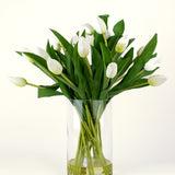 Het Zijden kunstboeket Tulpen in vaas Wit heeft witte tulpen met groene bladeren en stelen in een heldere glazen vaas, tegen een eenvoudige lichte achtergrond.